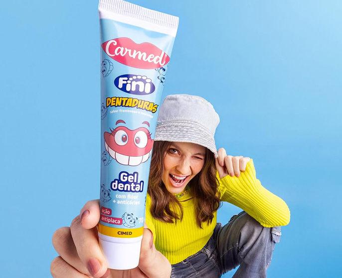 Gel dental Carmed Fini Dentaduras segurado por jovem sorridente