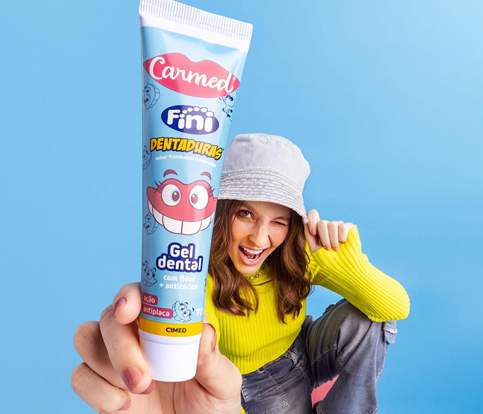 Gel dental Carmed Fini Dentaduras segurado por jovem sorridente