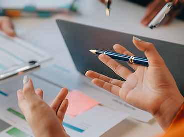 Mãos gesticulando enquanto pessoas discutem relatórios e apresentam ideias