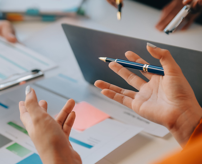 Mãos gesticulando enquanto pessoas discutem relatórios e apresentam ideias