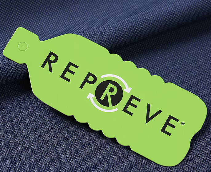 Tag verde REPREVE aplicada sobre tecido azul, destacando o uso de material sustentável reciclado
